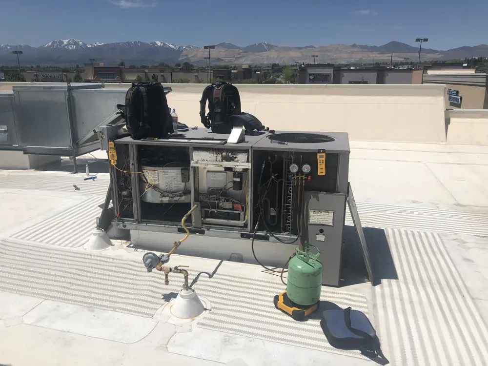 Technician servicing a commercial rooftop unit with snow-capped Wasatch peaks in the distance