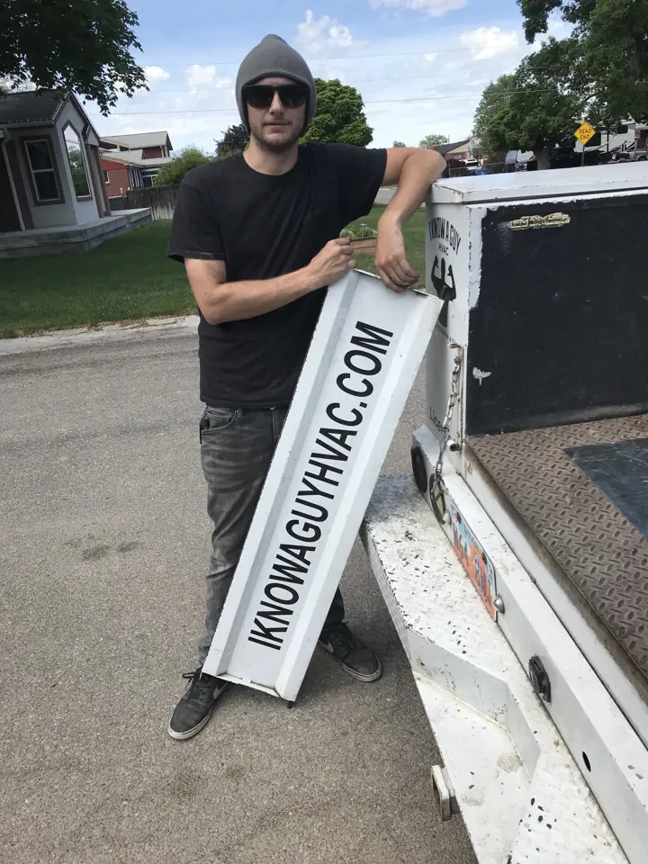 I Know A Guy HVAC team member holding an IKNOWAGUYHVAC.COM sign at the service truck