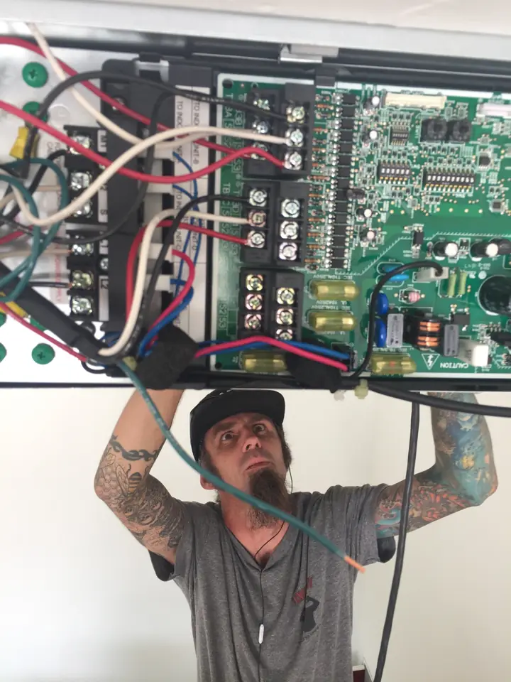 Technician troubleshooting an HVAC control board overhead