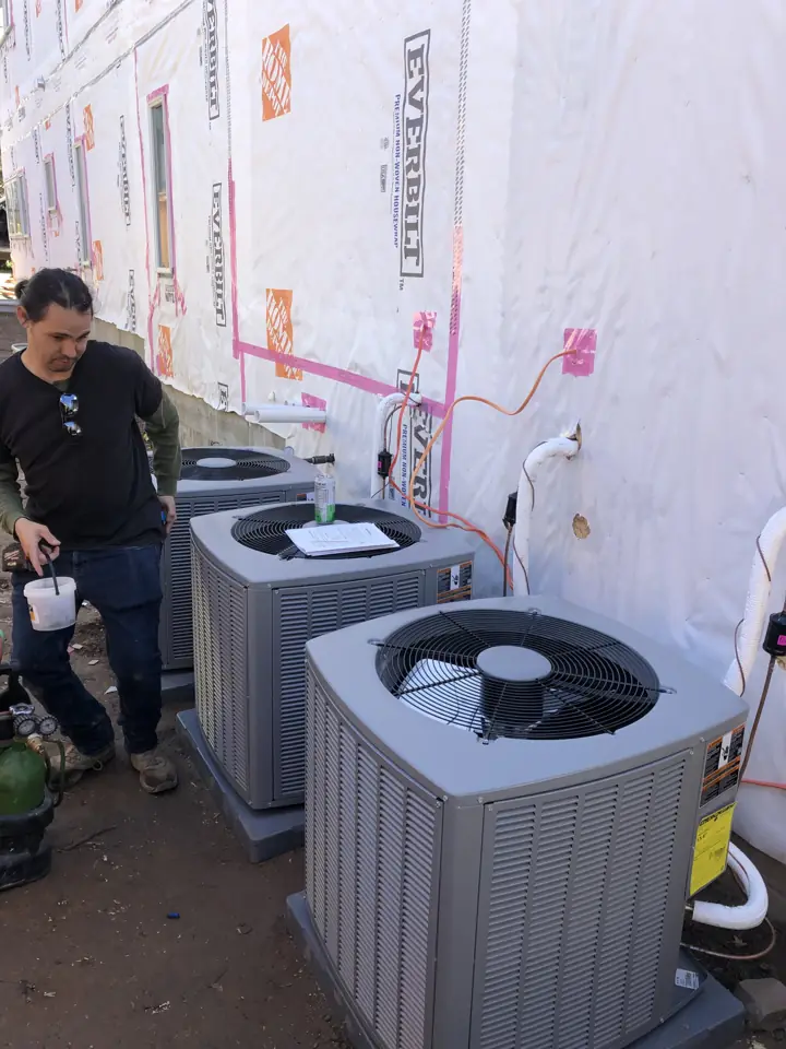 Technician finishing two new AC condensers at a new-construction home